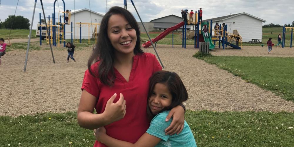 Angelica Cornejo, 22, being embraced by a student on the playground of Mamawi Atosketan Native School in the Canadian province of Alberta. (Andrew McChesney / Adventist Mission)