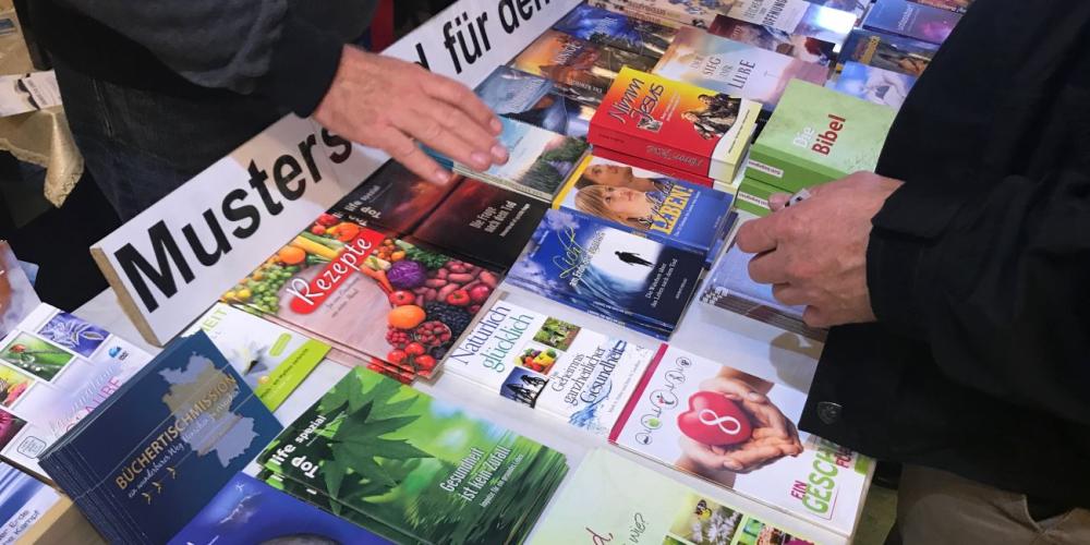 A man, right, browsing Adventist literature at the Naumann family book booth at an Adventist Theological Society youth convocation near Hanover, Germany, in October 2017. (Andrew McChesney / Adventist Mission)