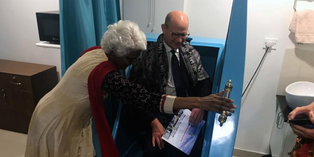 Dr. Daisy Rani Rao helping Adventist Church president Ted Wilson into a hydrotherapy steam chamber during a tour of the new Vibrant Life Medical and Wellness Clinic in Bengaluru, India, on Feb. 10, 2018. (Andrew McChesney / Adventist Mission)