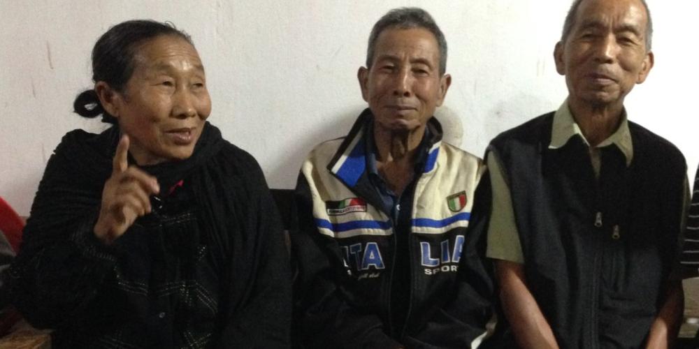 Makukhonna Panmei, left, talking as her husband, Panmeichung, center, and Amunang Gonmei listen on the porch of a home in the village of Samziuram in India's Nagaland state. The two men were handcuffed together during difficult times about 45 years ago. (Andrew McChesney / Adventist Mission)