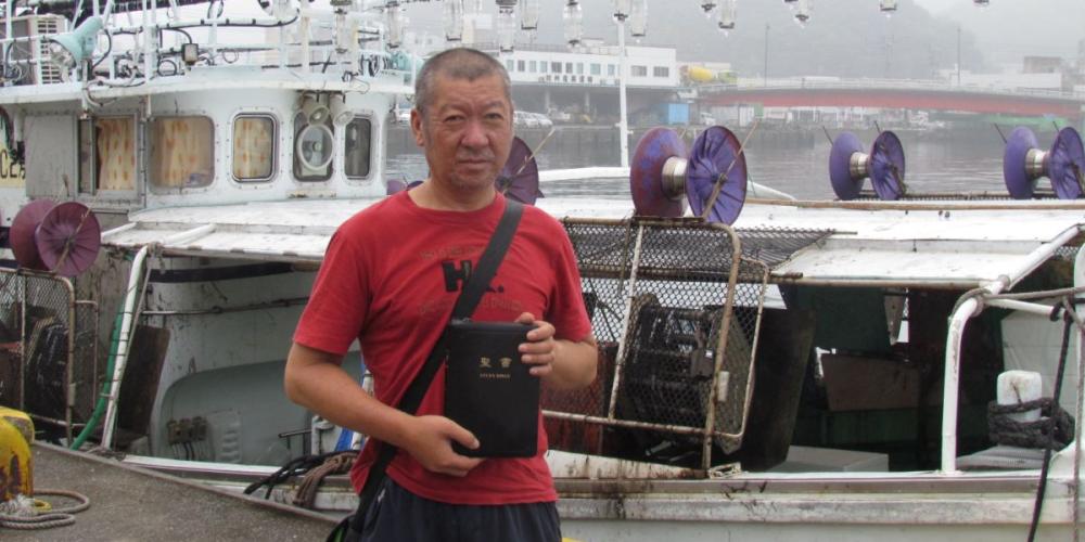 I first met Kojima Sadayuki, pictured holding his Bible at a seaport, when he asked me for a cigarette in a parking lot on the Japanese island of Tsushima. (Photos courtesy of Kurihara Kimiyoshi)