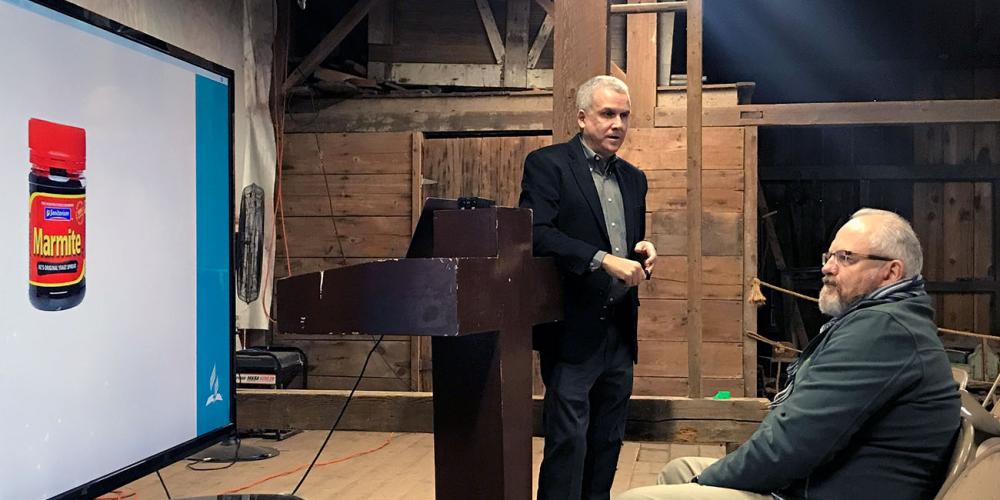 Adventist Mission director Gary Krause speaking about mission development in an old barn in the Historic Adventist Village in Battle Creek, Michigan, during LEAD Conference on Oct. 12, 2018. Seated is Jonathan Duffy, president of ADRA International. (Andrew McChesney / Adventist Mission)