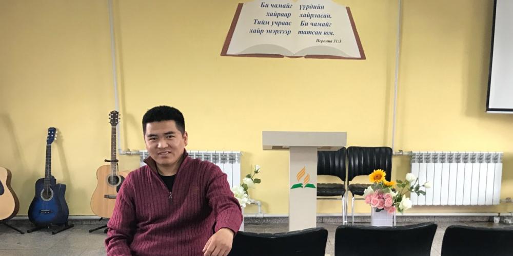 Global Mission pioneer Batzul Ganbold, 30, speaking in an interview in the Adventist church in Nalliah, a suburb of Ulaanbaatar, Mongolia. The Bible verse behind him reads, “Yes, I have loved you with an everlasting love; therefore with lovingkindness I have drawn you” (Jeremiah 31:3, NKJV).  (Andrew McChesney / Adventist Mission)
