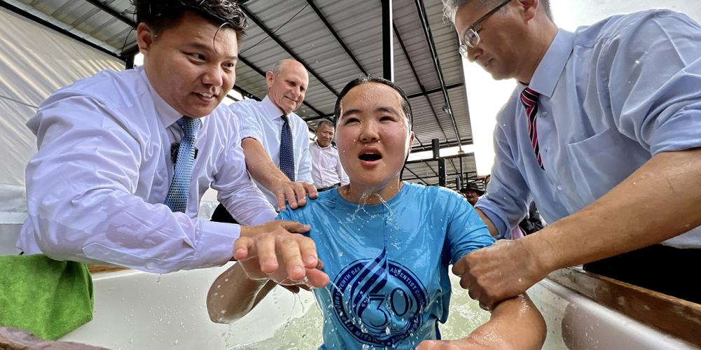Mongolia Mission president SukHee Han, right, and a local Mongolian pastor, L. MunkhOrgil, raising a newly baptized believer out of the water as General Conference president Ted N.C. Wilson watches on Sabbath, August 27, 2022, at a youth camp on the outskirts of Ulaanbaatar, Mongolia. Photo: Henry Stober