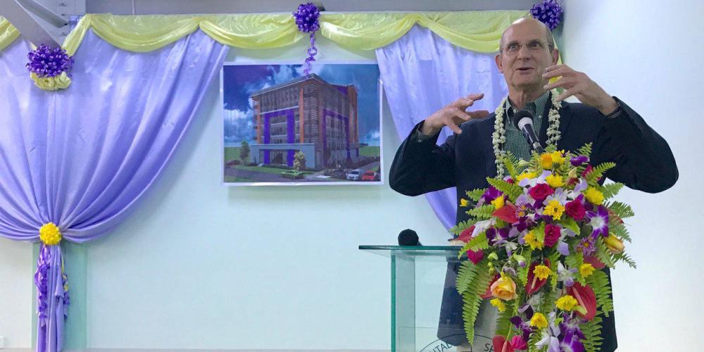 Ted N.C. Wilson, president of the Adventist world church, speaking at the dedication of a new school building in Yangon, Myanmar, on Nov. 9, 2017. A picture of the completed building is hanging on the wall. (Andrew McChesney / Adventist Mission)
