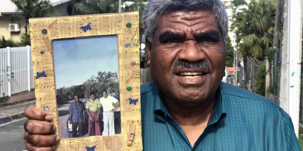 Felix Wadrobert, 59,  holding a photo of himself when he was 17. He is standing in the center in the photo with his father and another relative. (Andrew McChesney / Adventist Mission)