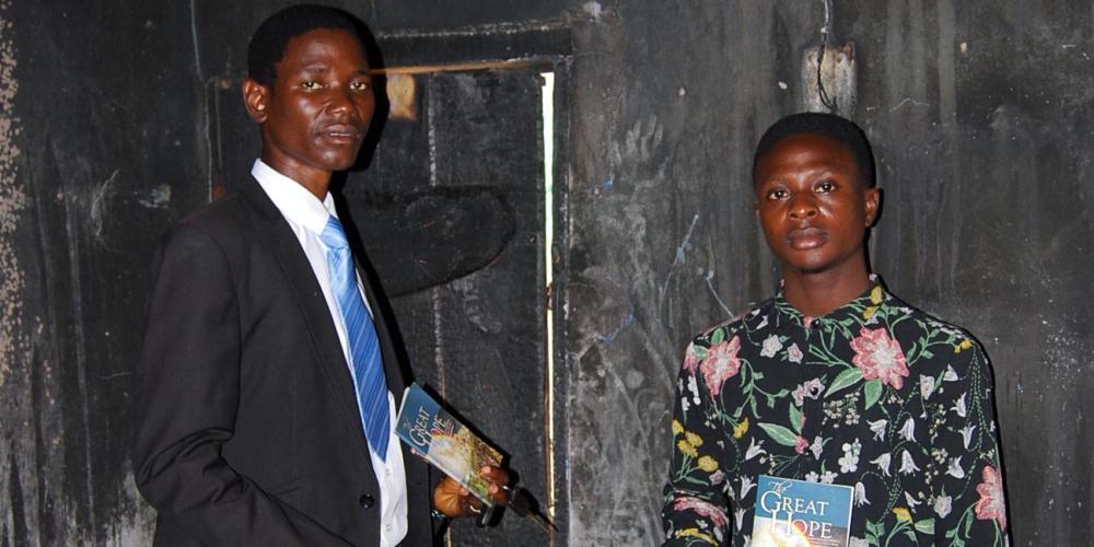 Nigerian student Olajide Oluwatobi Igbinyemi, right, holding his undamaged copy of “The Great Hope” in his fire-gutted apartment in Ede, Nigeria. Beside him is a local Adventist pastor. (Osun Conference / Adventist Mission)