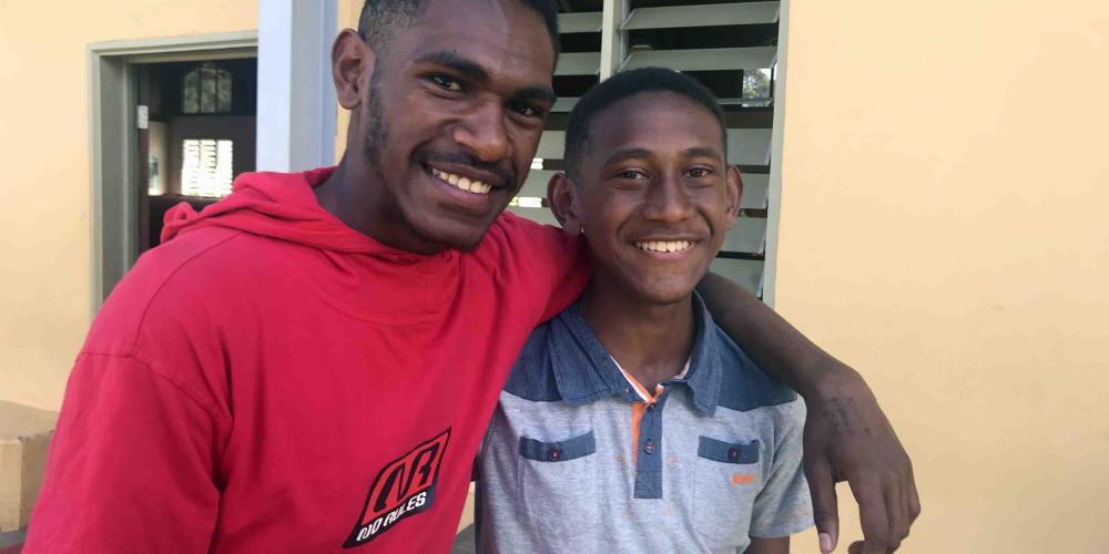 Rohi Goiye, left, embracing his best friend, Dwight Ope, outside Kama Seventh-day Adventist Church in Goroka, Papua New Guinea. (Andrew McChesney / Adventist Mission)