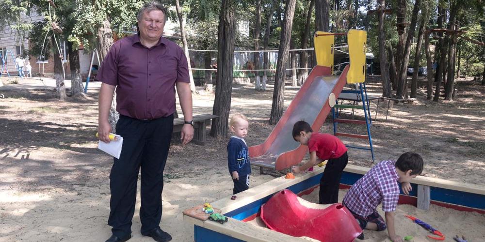 Andrey Prokopev, 43, watching his blond son play with other children in a sandbox at a summer camp in southern Russia. (Andrew McChesney / Adventist Mission)