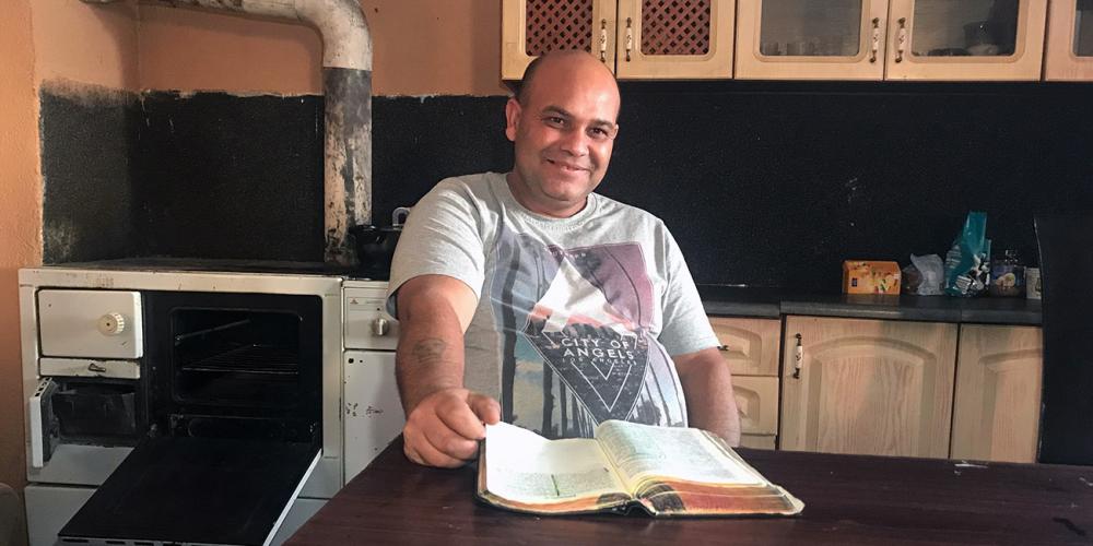 Peter Mižigar, 44, sitting at his kitchen table with the Bible where he found the Sabbath in the Roma settlement of Rakúsy, Slovakia. (Andrew McChesney / Adventist Mission)