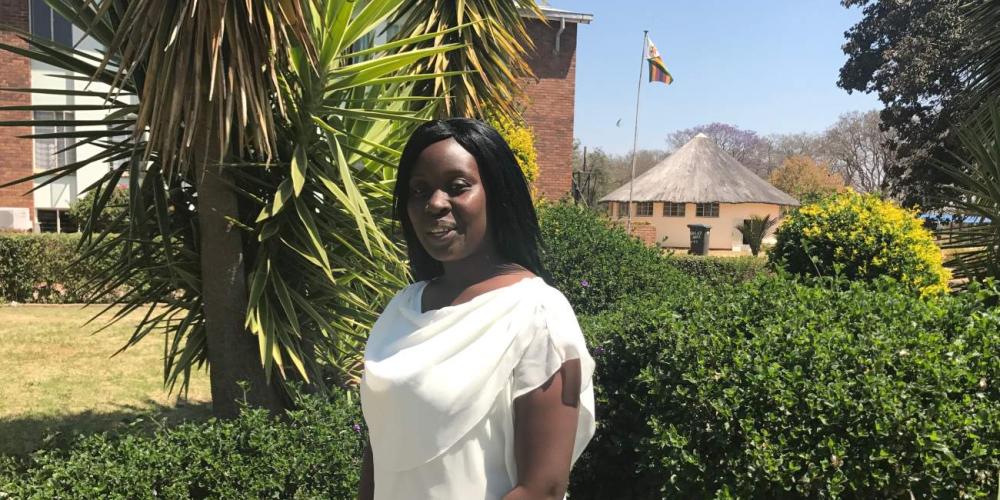 Hazel Moyo, 23, meeting with Adventist Mission on the campus of Solusi University near Bulawayo, Zimbabwe. The Zimbabwe flag is waving in the background. (Andrew McChesney / Adventist Mission)