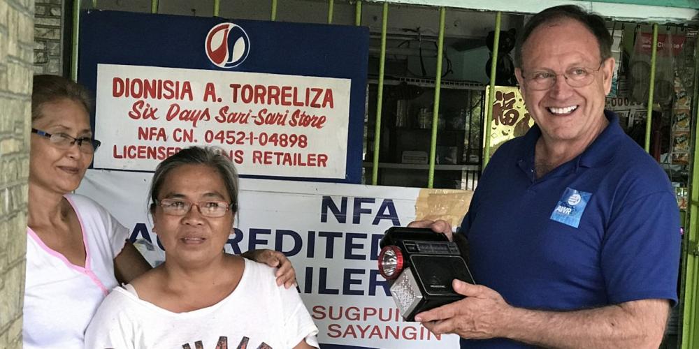 Duane McKey, right, holding a radio outside the Six Days Sari-Sari Store in Calapan, Philippines. Villagers hike an hour down a mountain to listen to Adventist World Radio at the store. (Photos: AWR)