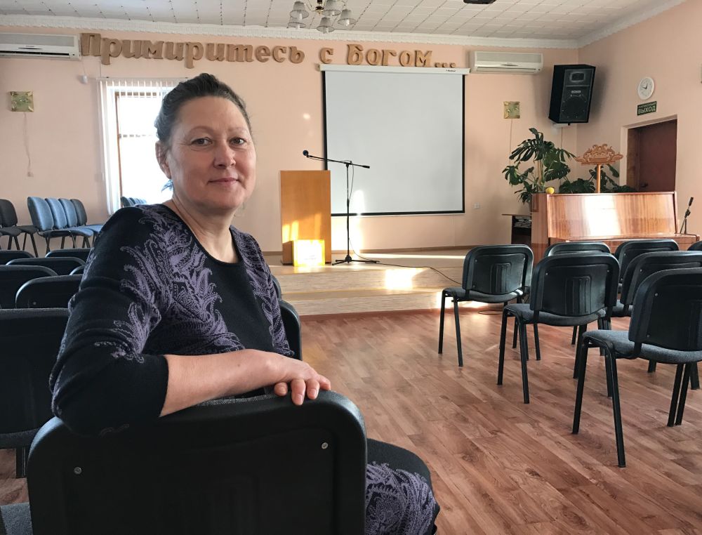 Valentina Shlee sitting in the sanctuary of the Southern Seventh-day Adventist Church in Pavlodar, Kazakhstan. The Russian words on the wall behind her read, "Be reconciled to God …" (Andrew McChesney / Adventist Mission)