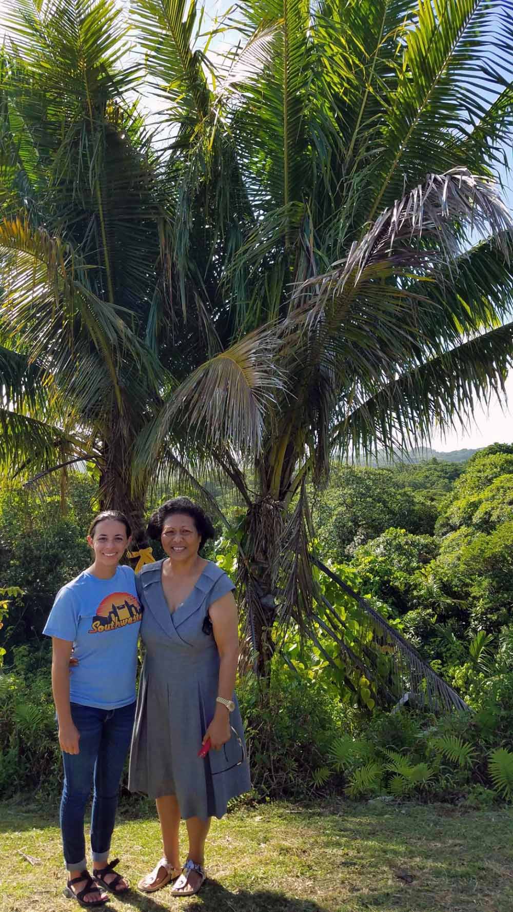 Melissa and Queen Bilung Gloria Salii standing near the two palm trees that the queen planted at the spot where Melissa was rescued at the age of 10.